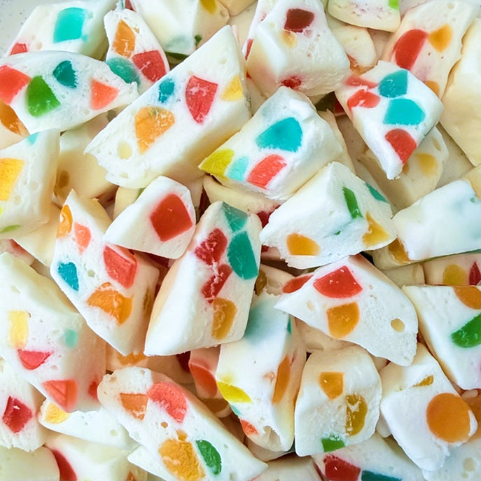 White chocolate candy melts or marshmallow candy pieces filled with colorful fruit pieces, shown in a close-up pile.